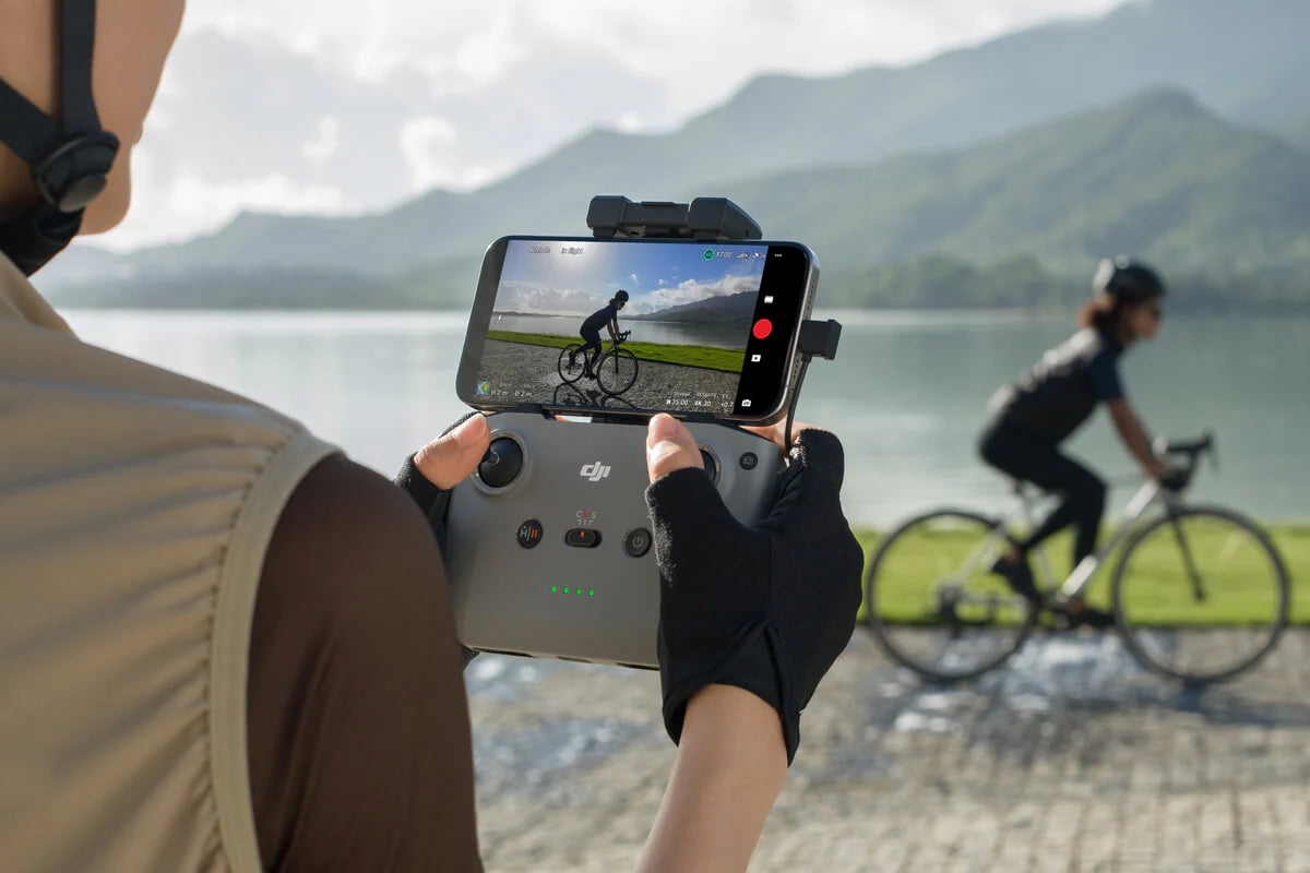 Person using DJI RC-N3 Remote Controller to film a cyclist by the water.